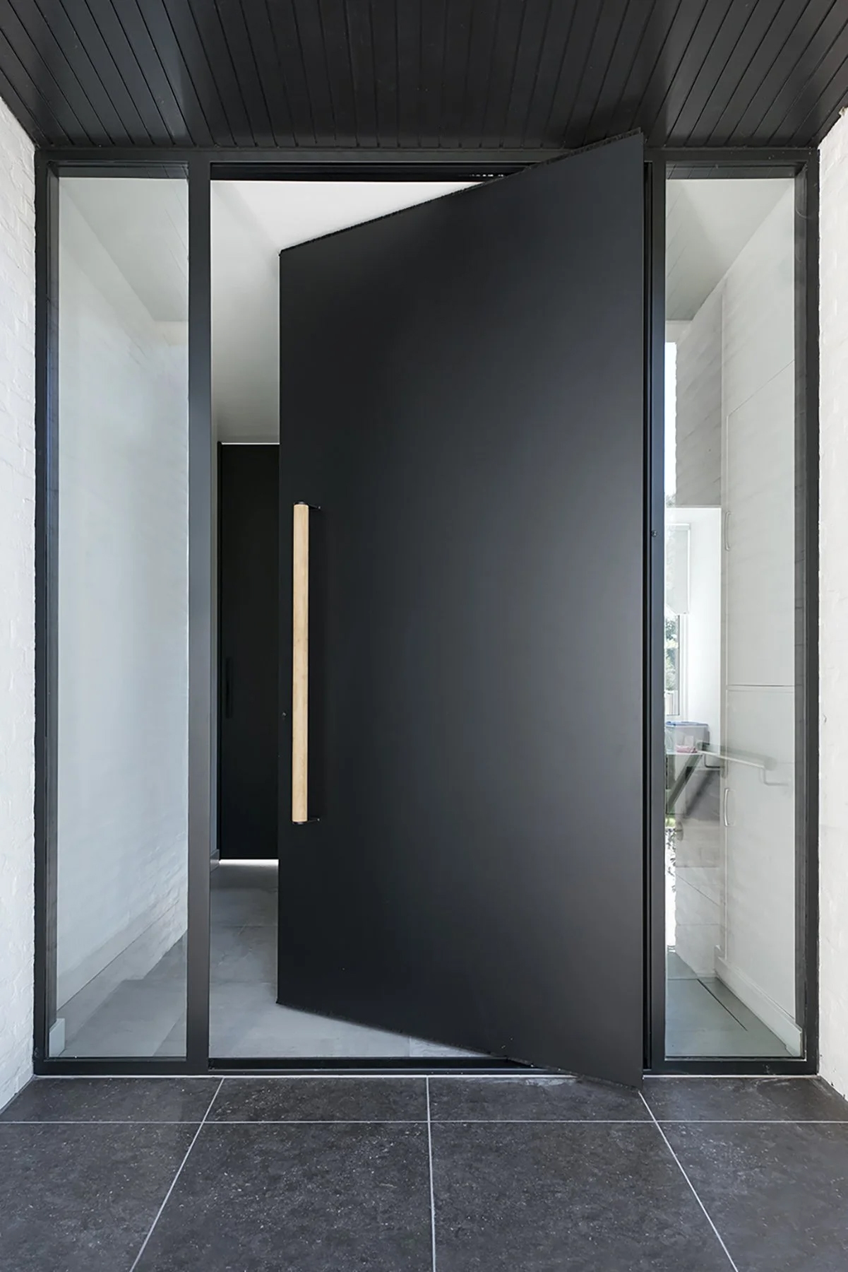 a black pivot door seen in the entrance to a minimal home